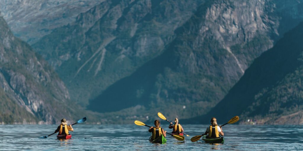 Four people in single kayaks on the fjord seen from the back. Photo_ Jon Hunnålvatn Tøn